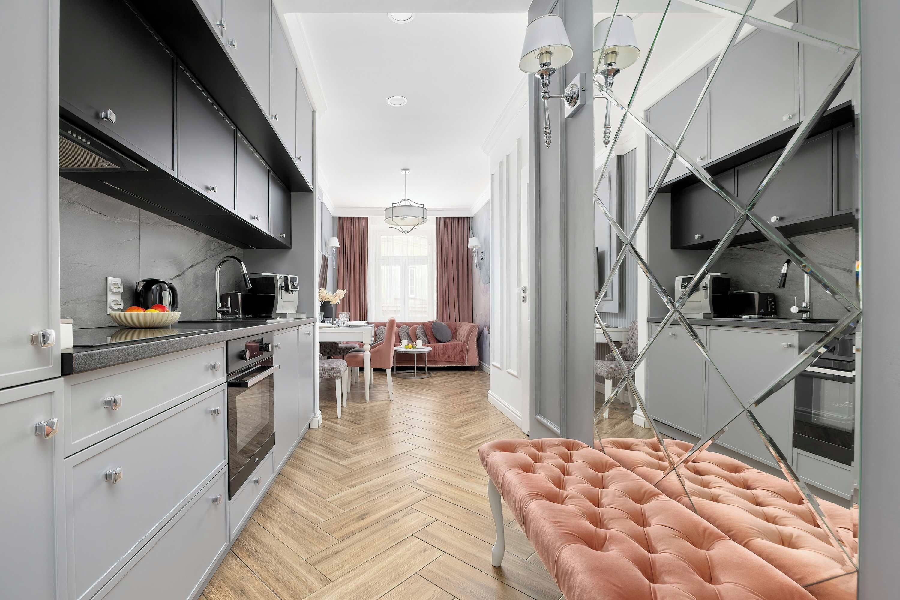 A modern kitchen with grey cabinetry, a wooden herringbone floor, and a pink upholstered bench.