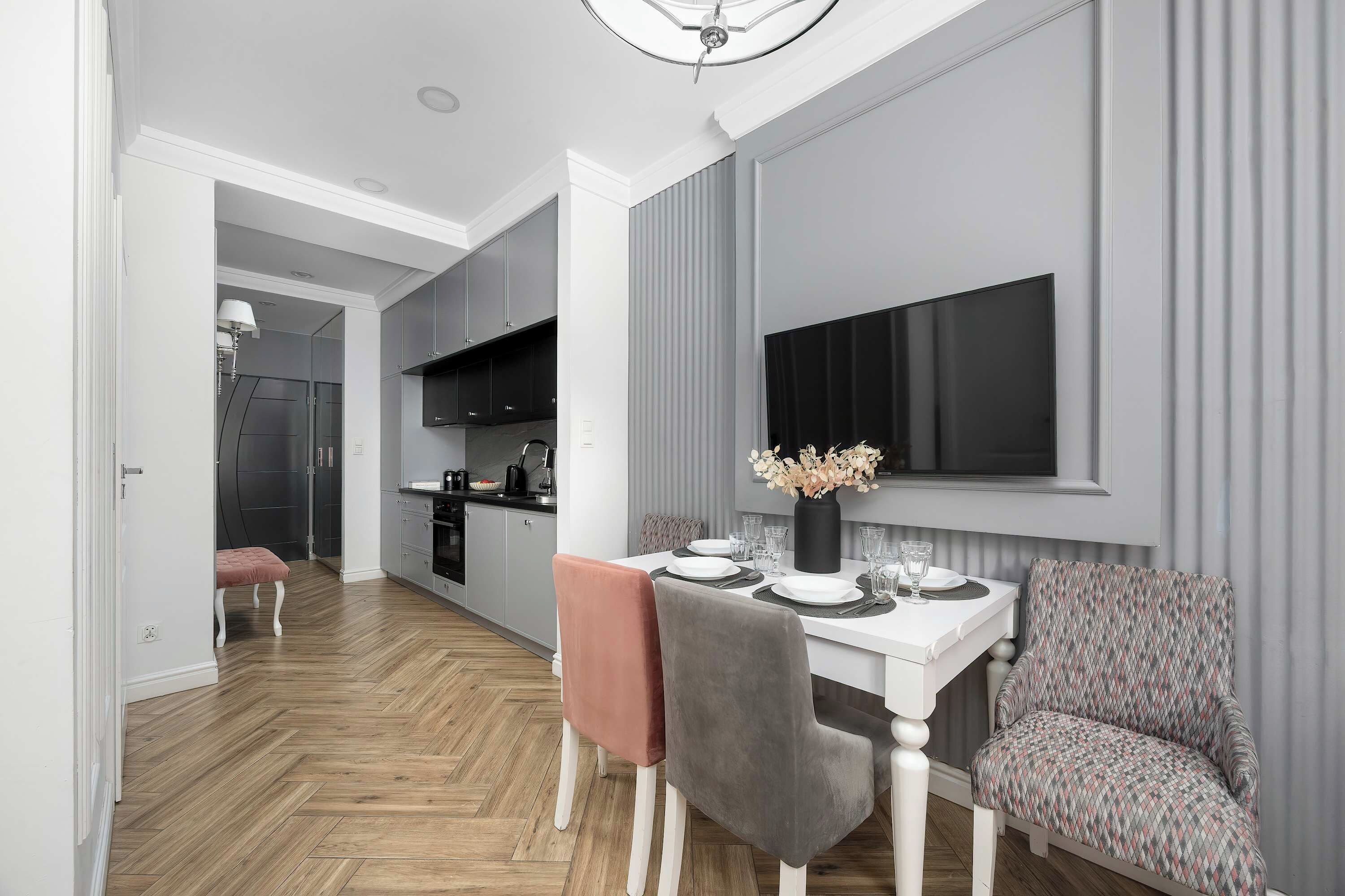 A modern dining area with a white table set for four, grey chairs, and a patterned sofa.