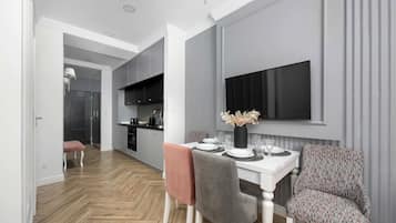 A modern dining area with a white table set for four, grey chairs, and a patterned sofa.