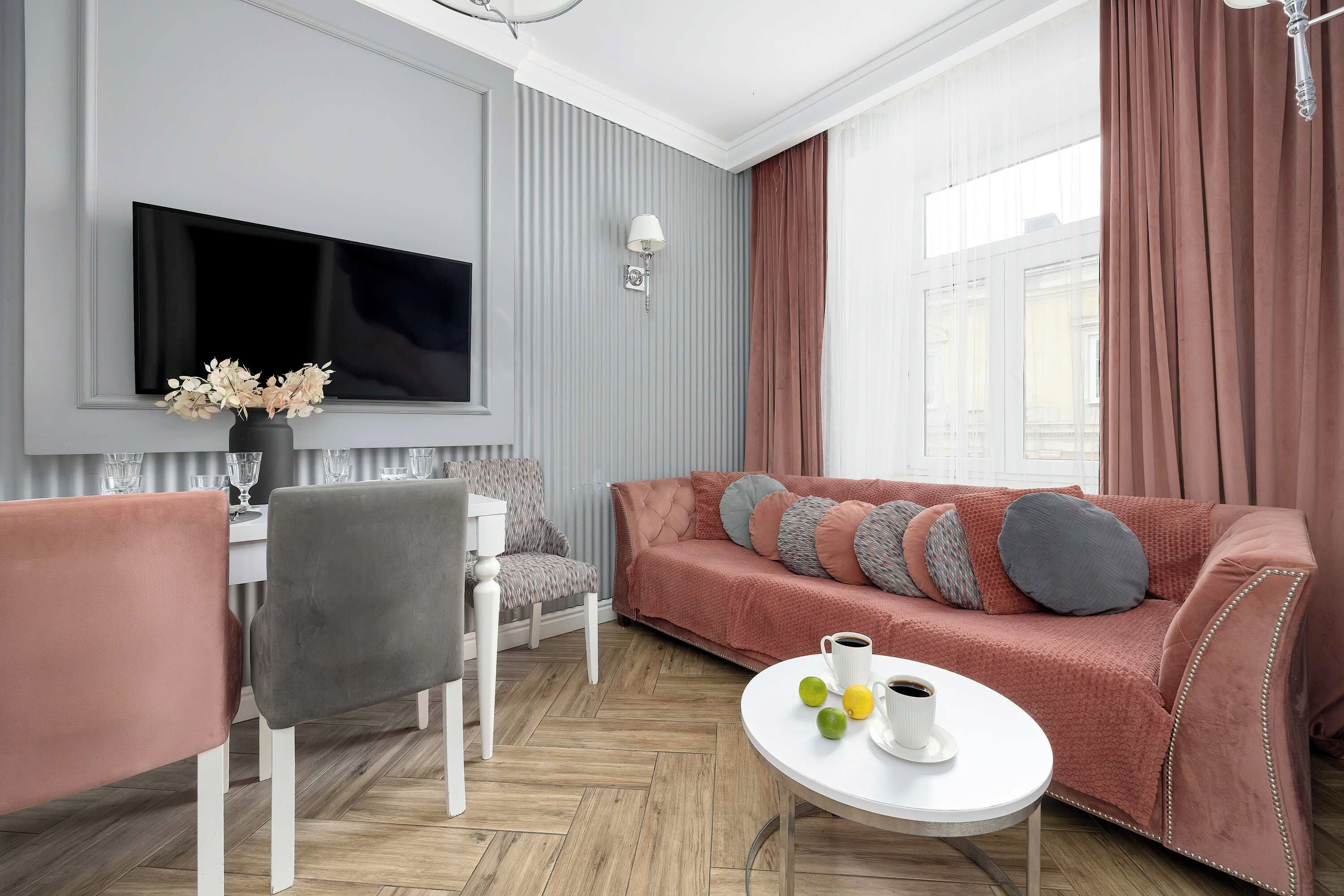 A modern living room with a flat-screen TV, a sofa with cushions, a dining table with chairs, and a coffee table with fruits and a cup.