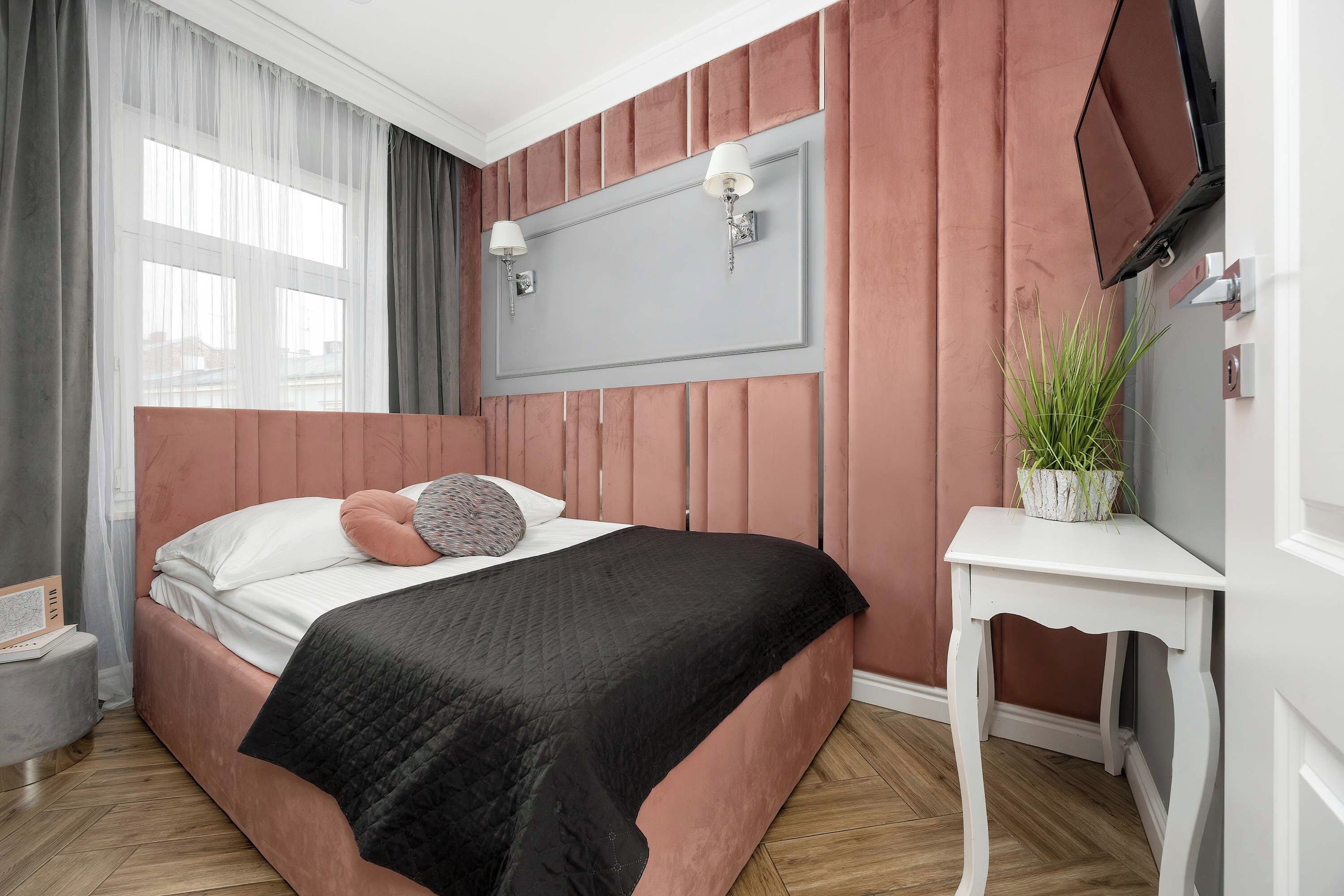 Ein Schlafzimmer mit einem Bett, einem Nachttisch, einer Topfpflanze und einem Fenster mit Vorhängen.