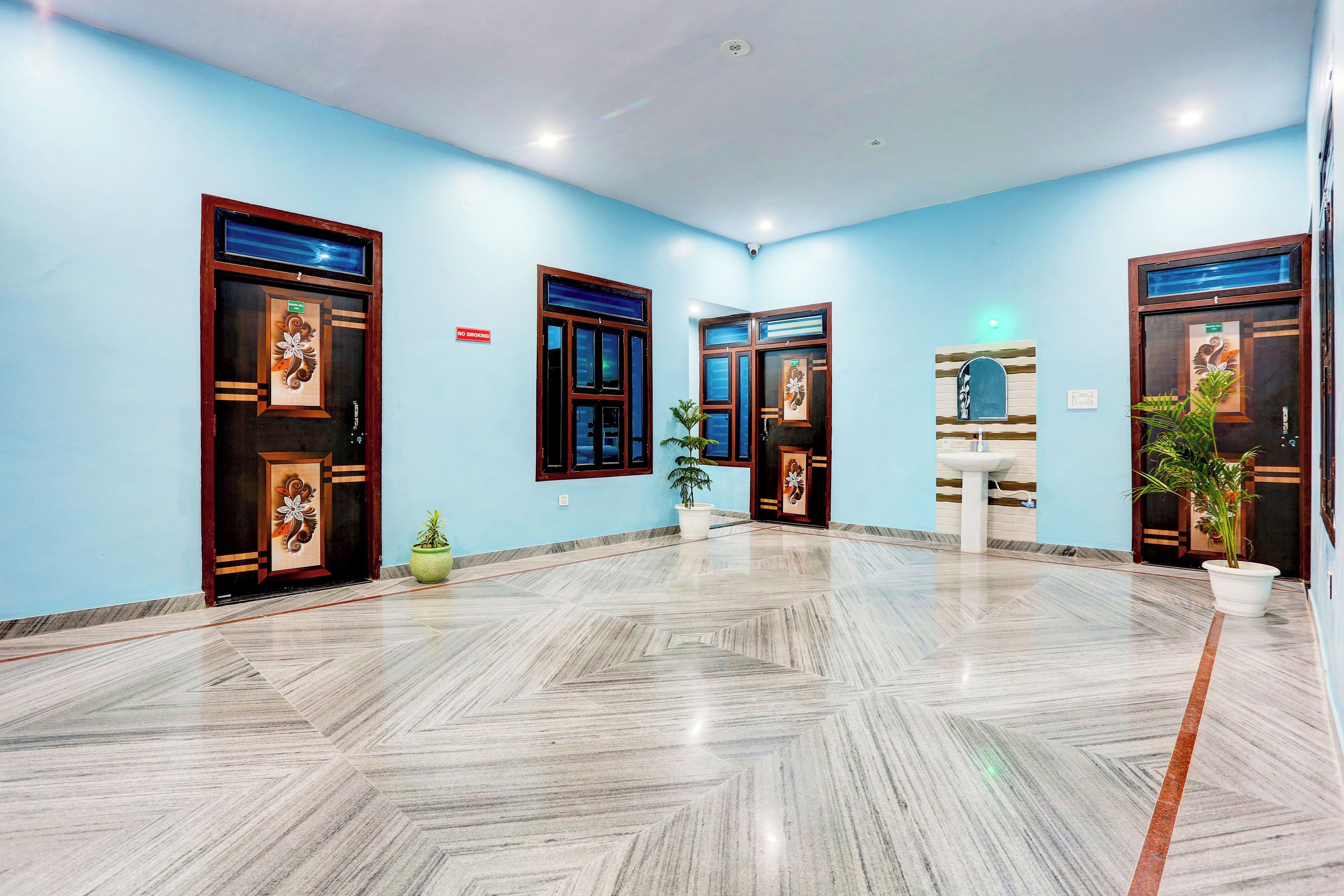 Um saguão de hotel com piso de mármore, quatro portas com painéis de vidro decorativos e plantas em vasos.