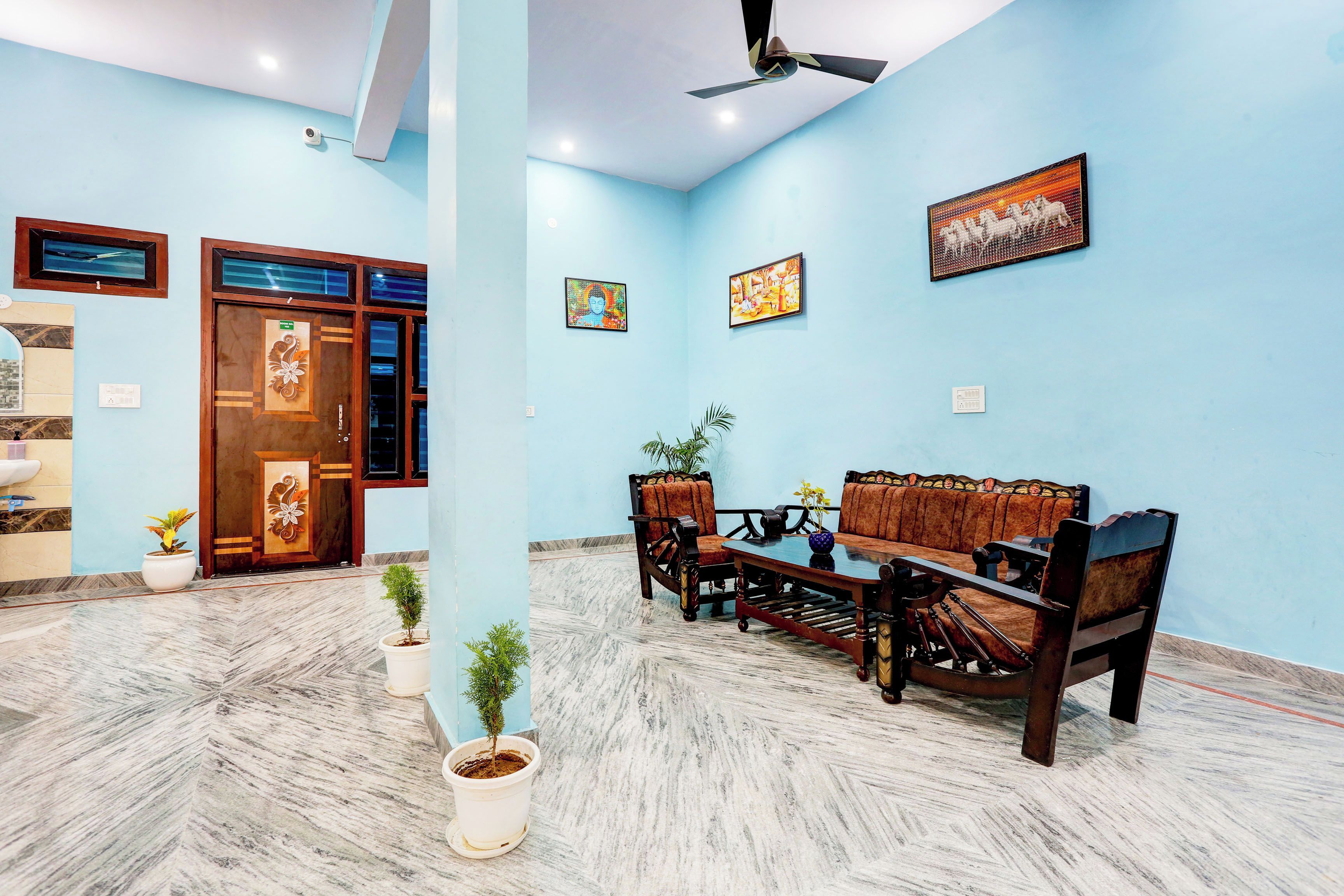 Quarto com parede azul, ventilador de teto, sofá, mesa de centro e porta com detalhe decorativo.