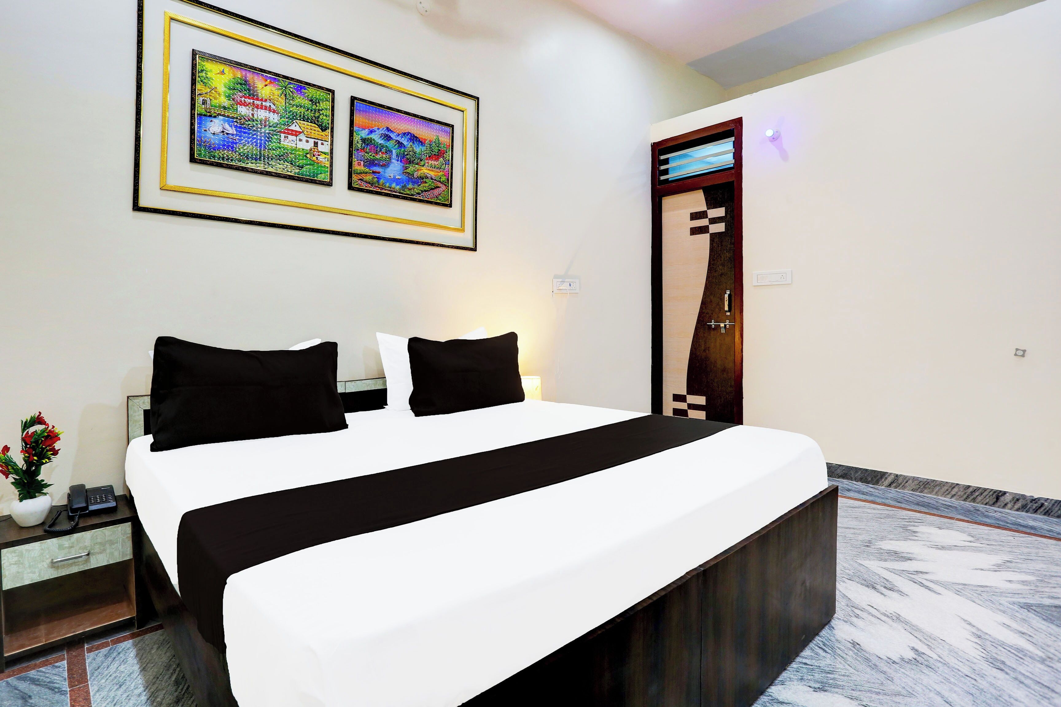 Quarto de hotel com cama, mesas de cabeceira, telefone e quadro na parede.