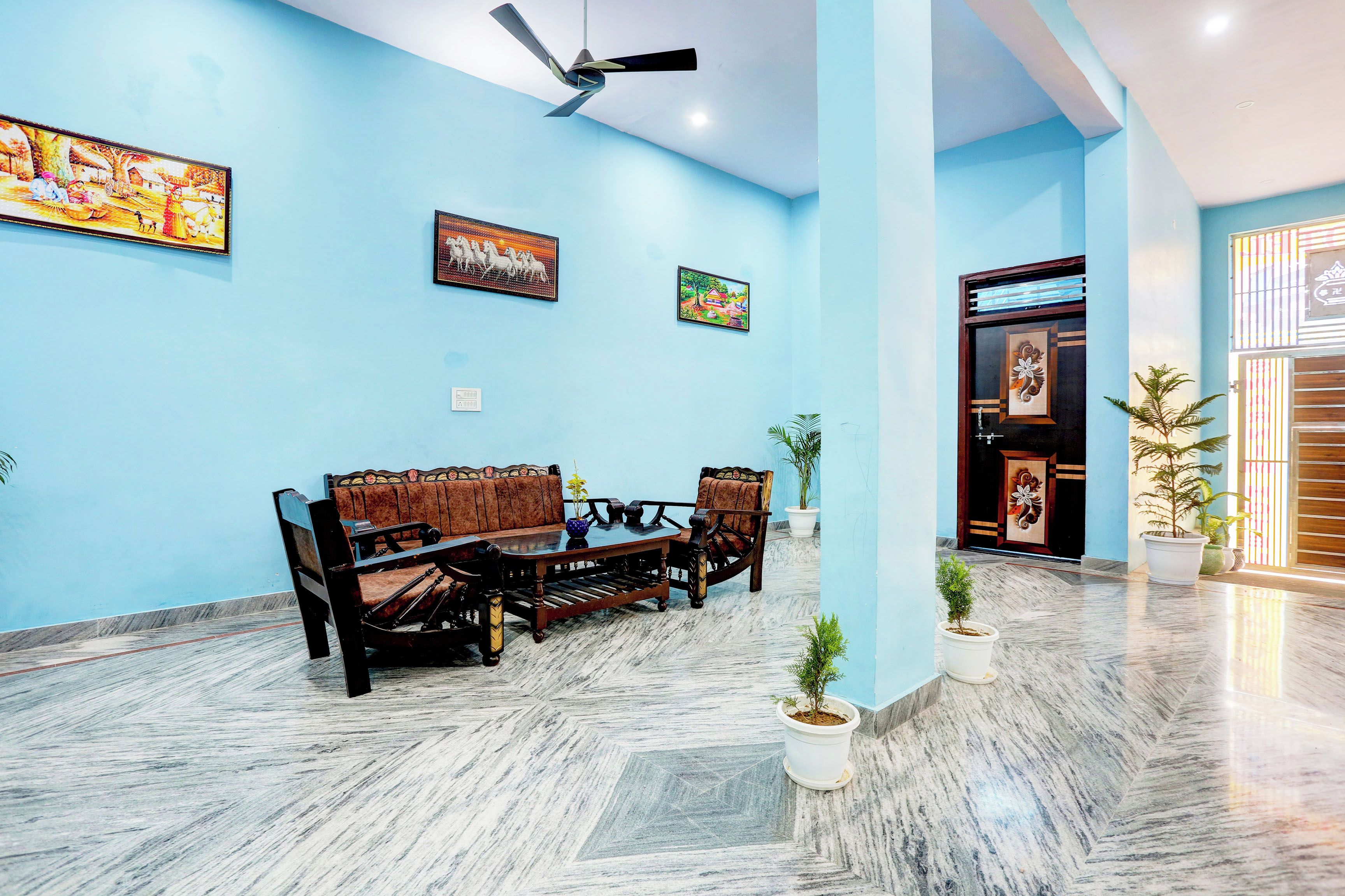 Um quarto amplo com parede azul, ventilador de teto, mesa de jantar com cadeiras e porta com painéis decorativos.