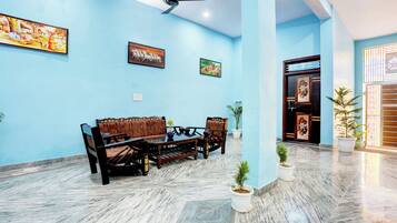 Um quarto amplo com parede azul, ventilador de teto, mesa de jantar com cadeiras e porta com painéis decorativos.