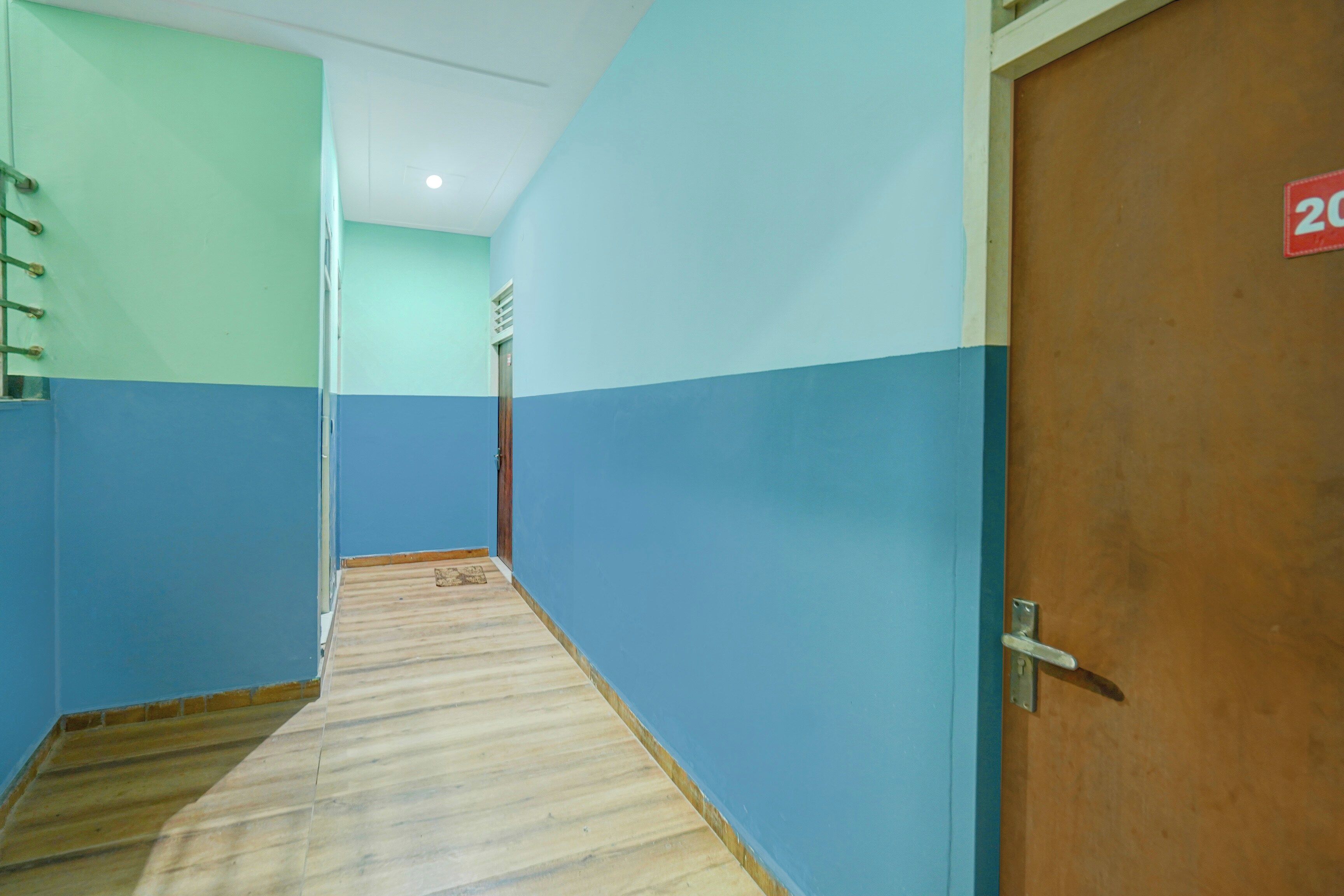 Um corredor com piso de madeira, parede azul e verde, e uma porta com o símbolo de número.