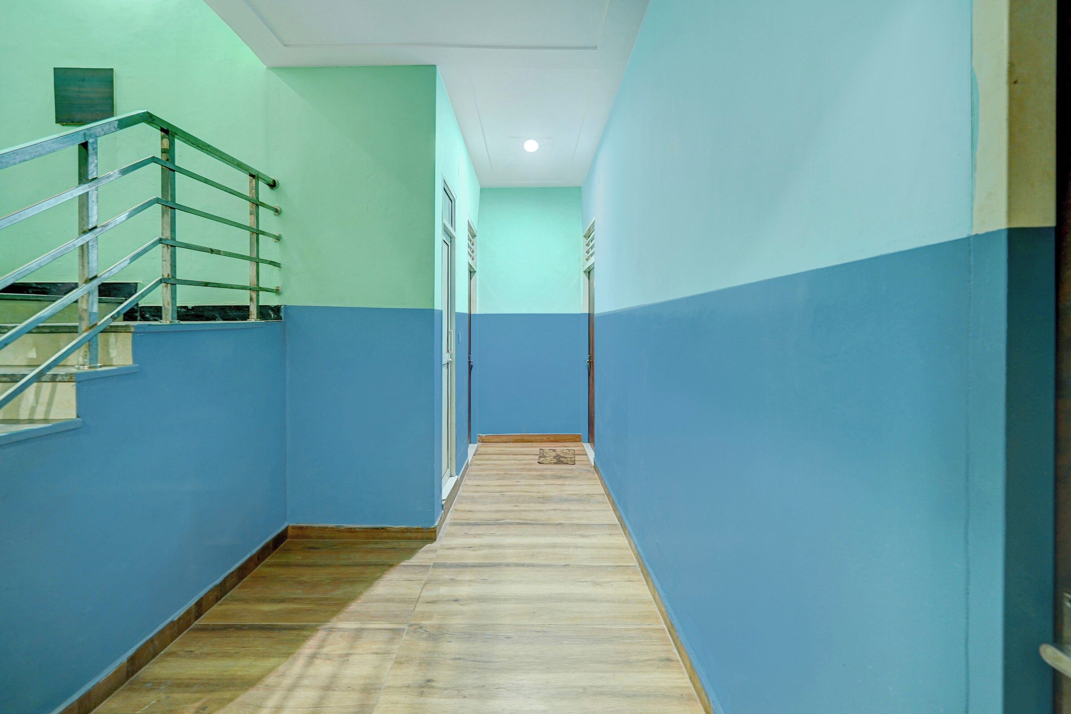Um corredor com piso de madeira, corrimão de metal e paredes pintadas em dois tons de azul.