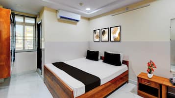A hotel room with a wooden bed, white bedding, a small wooden nightstand, a mirror, and a wall-mounted air conditioner.