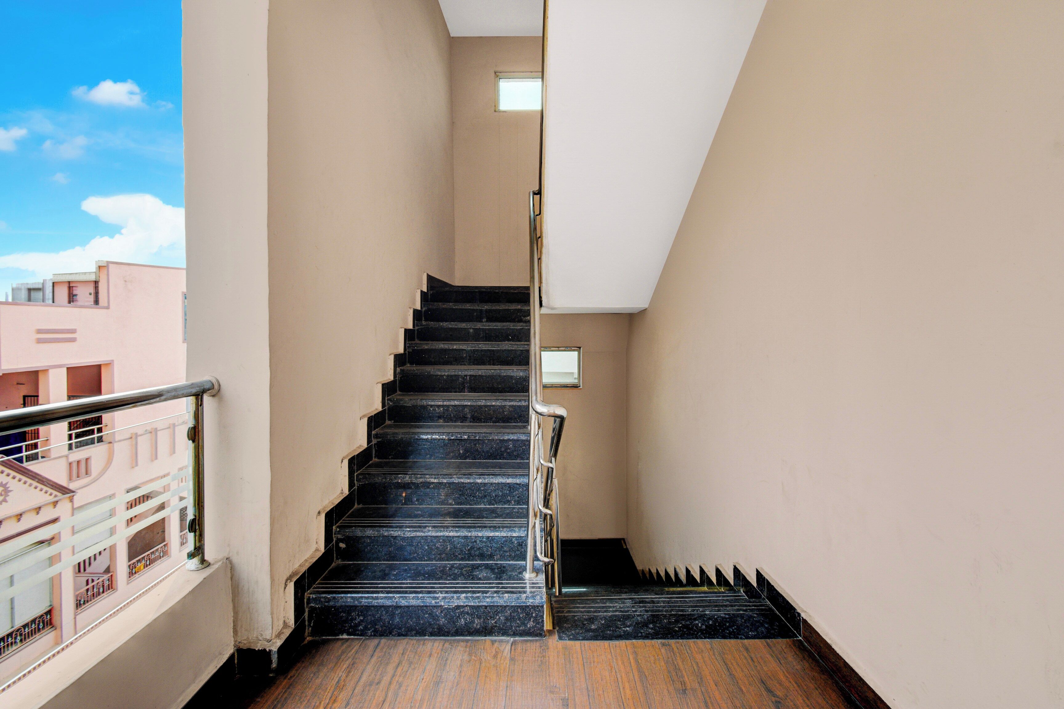 A narrow stairway with black steps leading to a landing, surrounded by plain walls and a metal railing on one side.