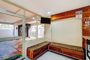 A hotel reception area with a glass door, a bench, a wall-mounted TV, and a wooden panel with a calendar. - Hotel O Mancherial Bus Terminal (Mancherial)