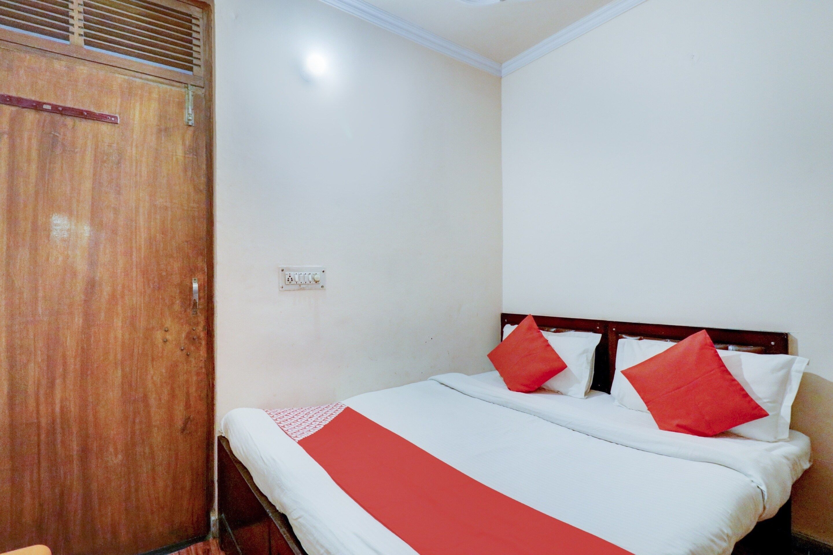 Una cama individual con cabecera de madera, ropa de cama blanca y dos almohadas rojas.