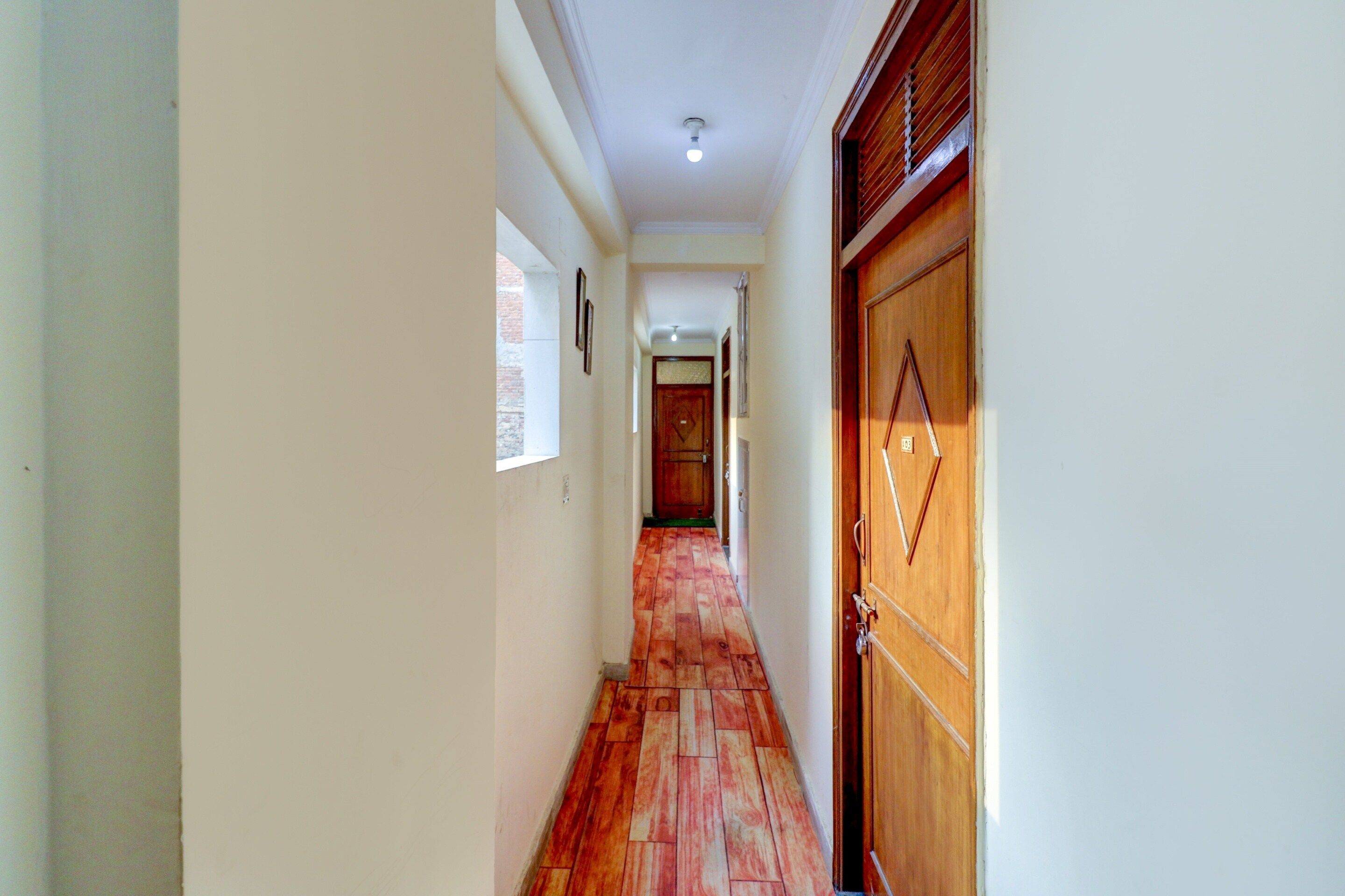 Un pasillo con una puerta de madera a la derecha, una ventana a la izquierda y otra puerta al final.