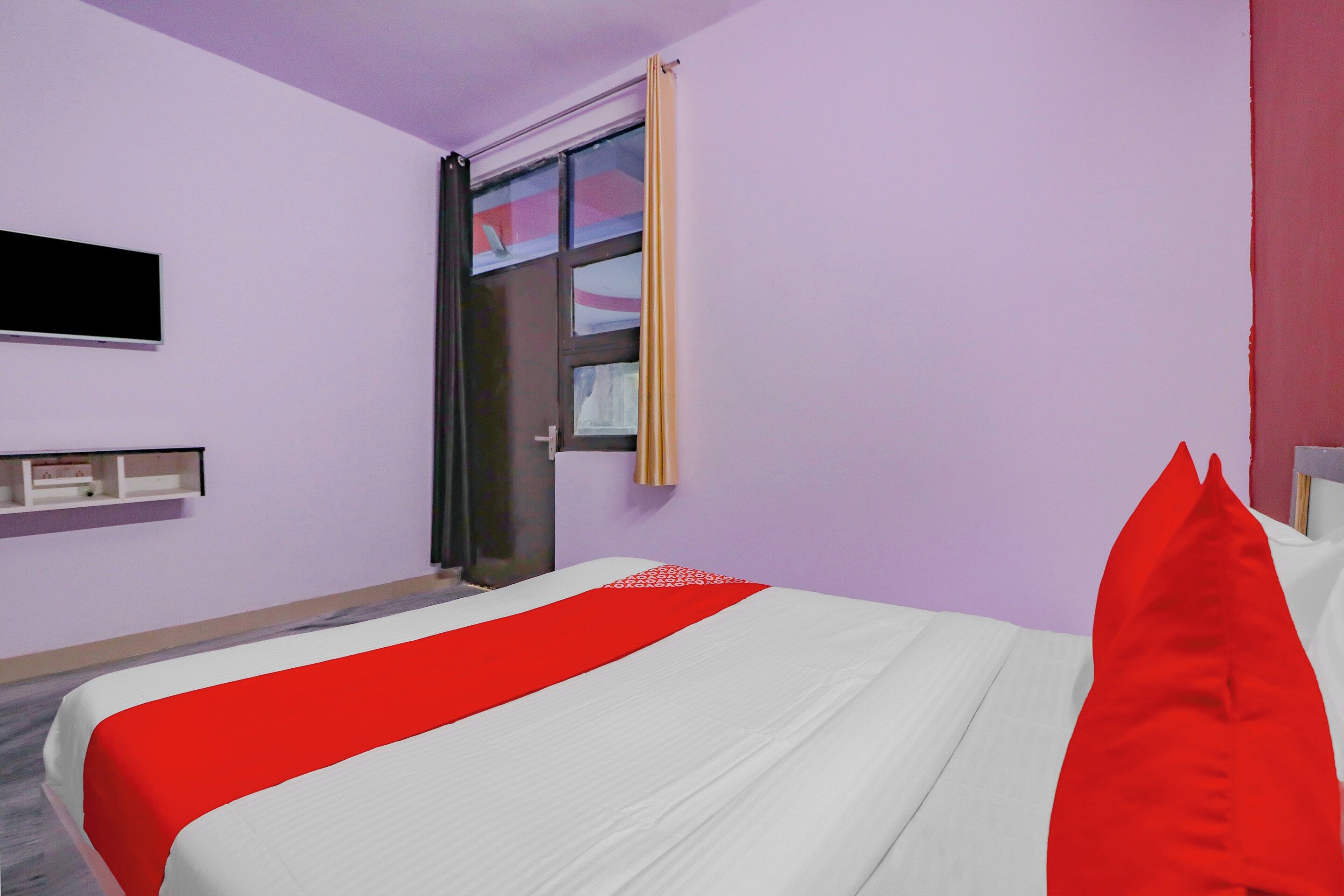 Une chambre d’hôtel avec un lit, un téléviseur fixé au mur et une fenêtre avec des rideaux.