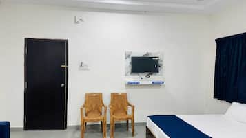 Habitación de hotel con cama, escritorio, dos sillas, televisor montado en la pared, ventilador de techo y una puerta.