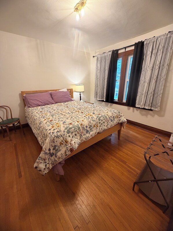 A bedroom with a wooden bed, a chair, a lamp, and a window with curtains.