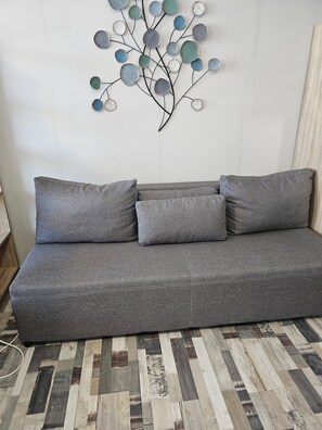 Ein graues Sofa mit drei Kissen vor einer Wand mit einer Zierdekoration aus Metall.