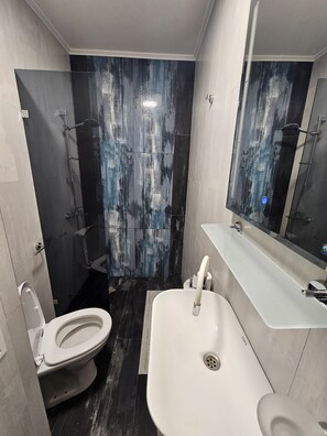 Ein modernes Badezimmer mit Toilette, Waschbecken, Dusche und Spiegel.