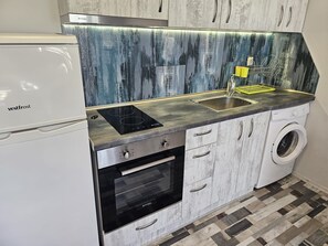 Eine kompakte Küche mit Kühlschrank, Herd, Backofen, Spüle und Waschmaschine.