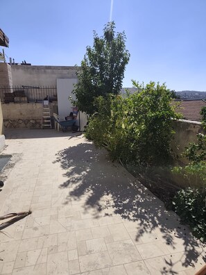 A rooftop patio with a tiled floor, a metal chair, a ladder, and a large tree providing shade.