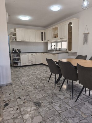 A kitchen with white cabinets, a dining table with chairs, and a tiled floor.