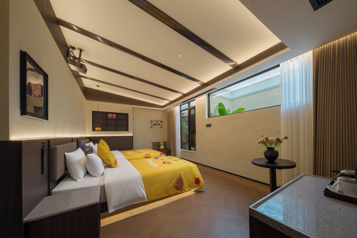 Een hotelkamer met een bed, nachtkastje en een kleintje tafeltje met een vaas.