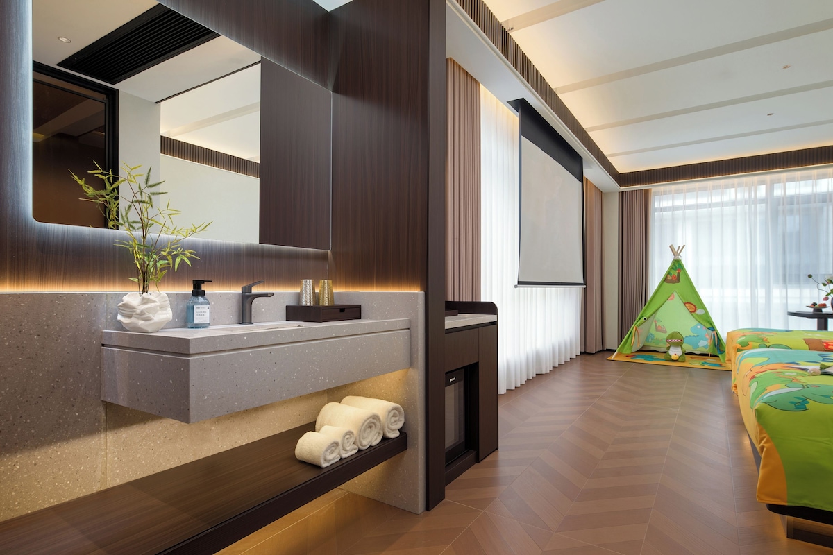 Een moderne hotelkamer met een grote spiegel, een ingebouwd kaptafel, een kleine open haard en een kinderspeelhoek met een tent.
