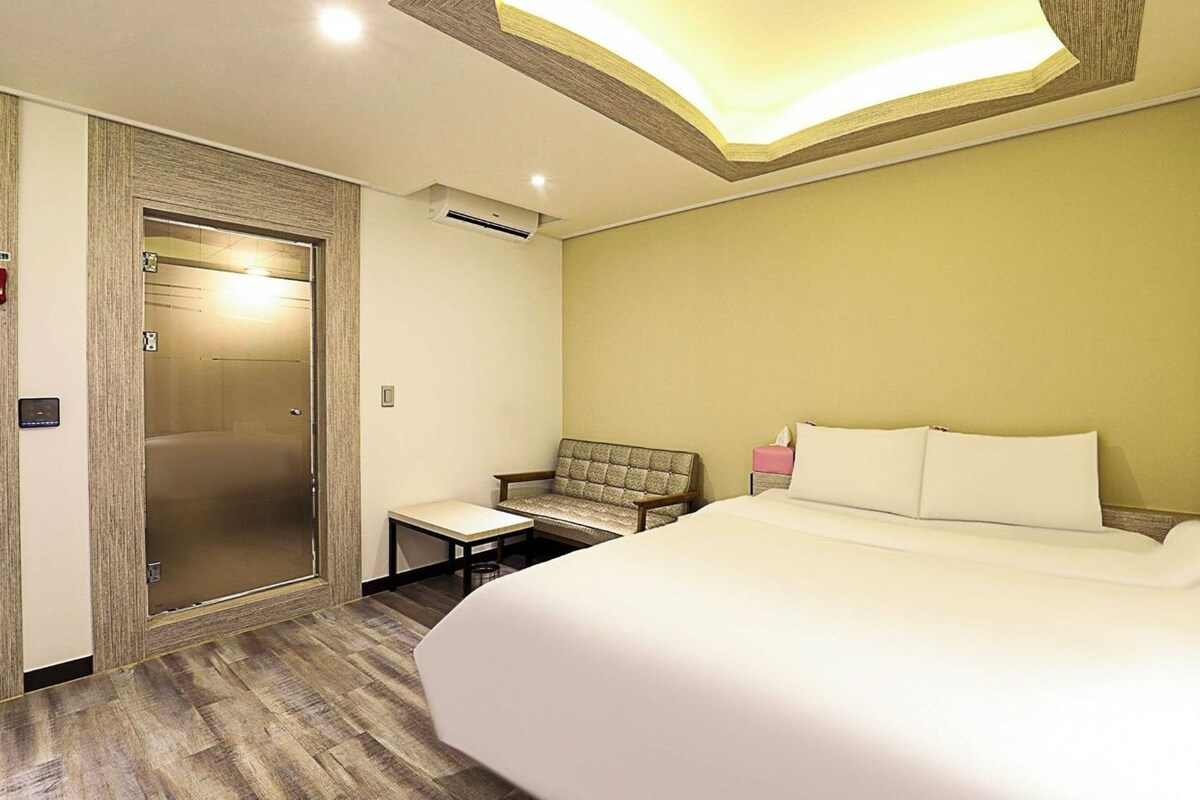 Ein Hotelzimmer mit einem Bett, einer Sitzecke und einer Tür zu einem Aufzug.