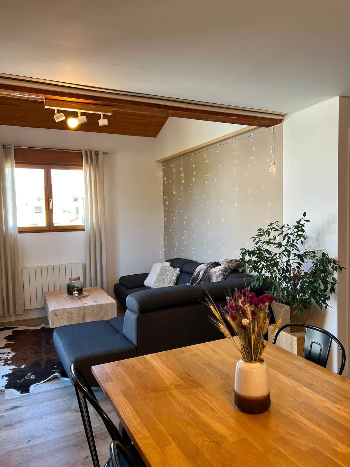Un salon moderne avec un canapé, une table basse en bois surmontée d’un vase, et une table à manger avec des chaises.