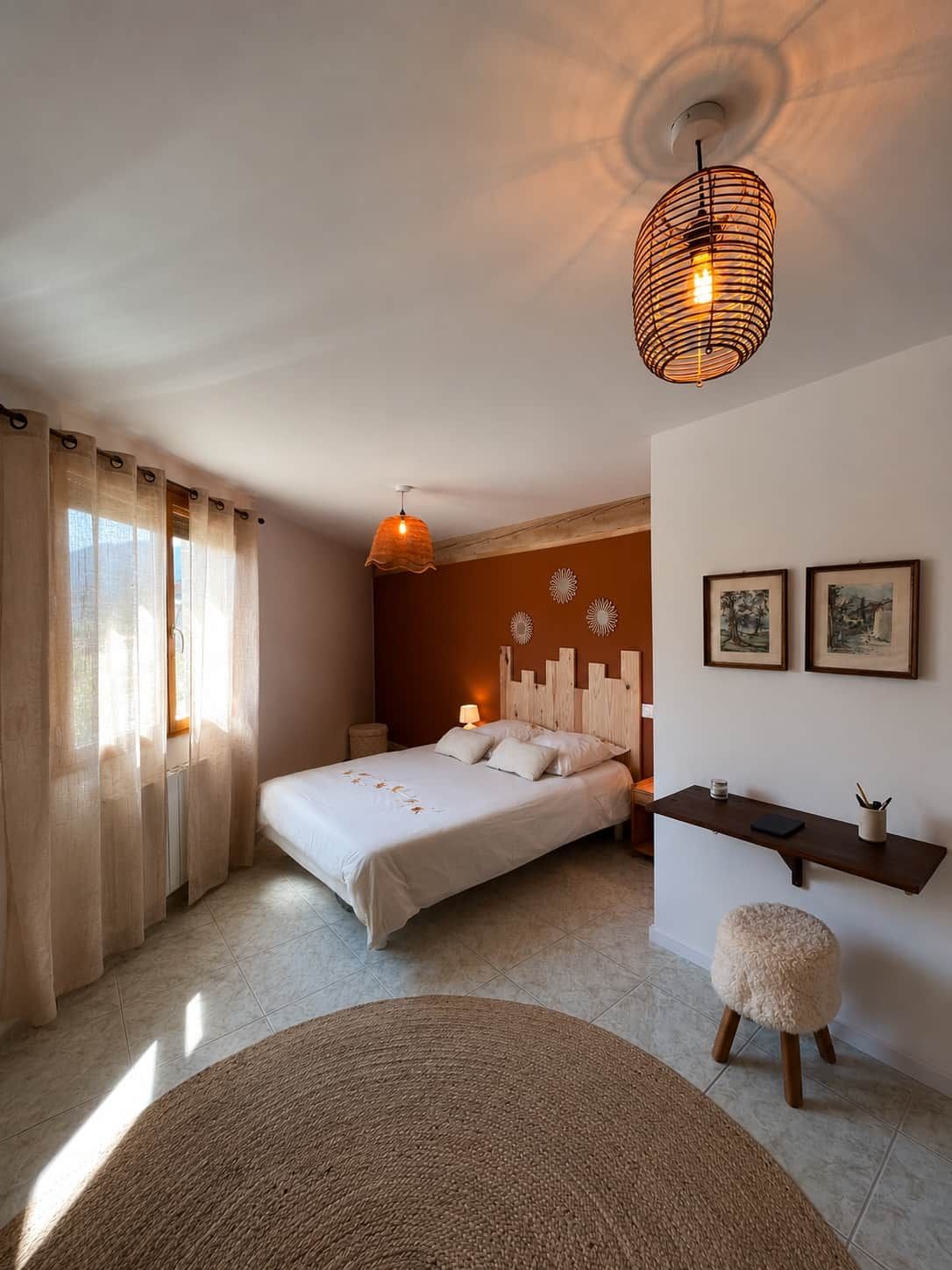 Ein Schlafzimmer mit einem Bett, einem Nachttisch, einer Lampe, einem runden Teppich, einem Hocker und einem Wandregal mit Bildern.