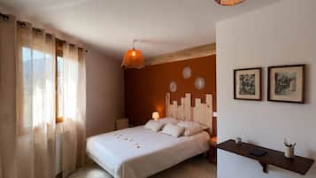 Ein Schlafzimmer mit einem Bett, einem Nachttisch, einer Lampe, einem runden Teppich, einem Hocker und einem Wandregal mit Bildern.