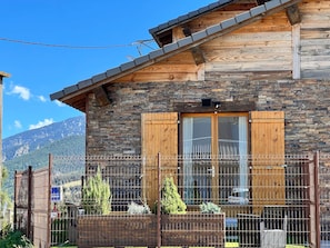 Una cabaña de madera con fachada de piedra, contraventanas de madera y un jardín vallado.