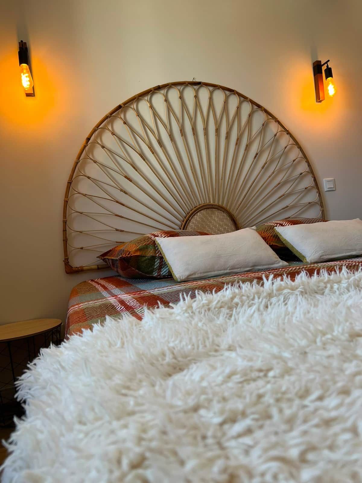 A bed with a large, round, woven headboard and two wall-mounted light fixtures.