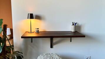 Une pièce dans laquelle on trouve une étagère en bois, sur laquelle sont posées deux œuvres d’art encadrées, une lampe et un petit tabouret.