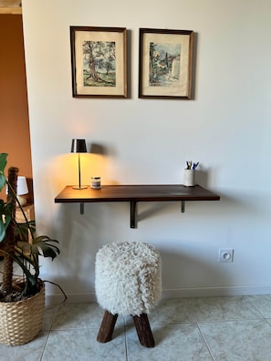 Ein Zimmer mit einem hölzernen Regal, das zwei gerahmte Kunstwerke, eine Lampe und einen kleinen Hocker beherbergt.