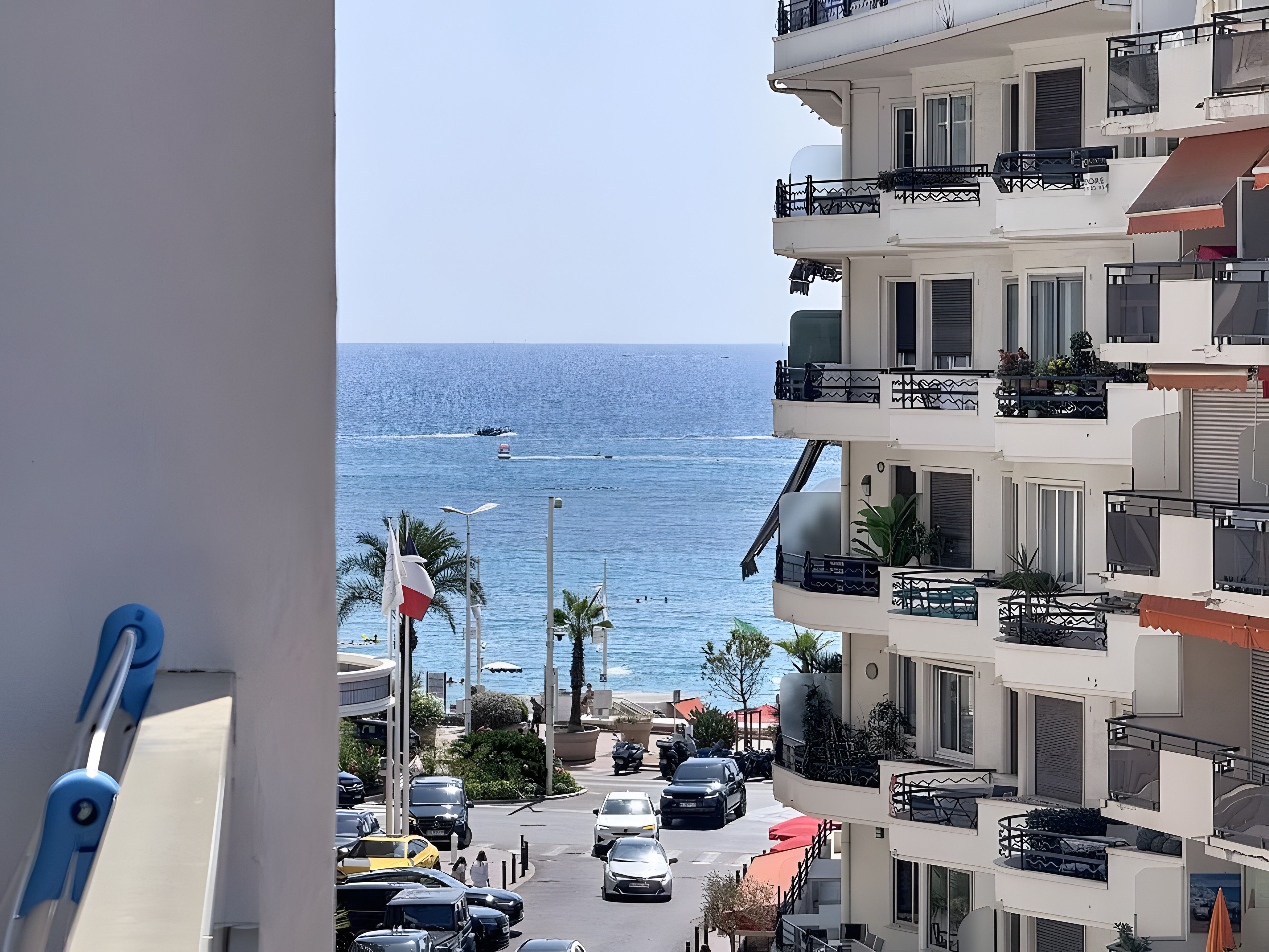 Vista di una strada costiera con una visuale aperta sul mare, auto parcheggiate e un edificio a più piani con balconi.