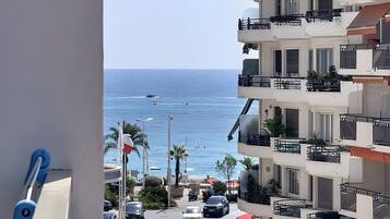 Vista di una strada costiera con una visuale aperta sul mare, auto parcheggiate e un edificio a più piani con balconi.
