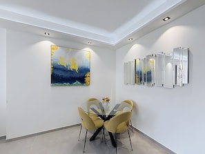 A modern dining area with a glass table, yellow chairs, a large abstract painting, and a series of mirrors on the wall. - Apartment 'Appartement 2 Pièces Cannes' with Sea View, Wi-Fi and Air Conditioning (Cannes)