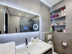 Un baño moderno con un espejo grande, un tocador con lavabo y una zona de ducha.