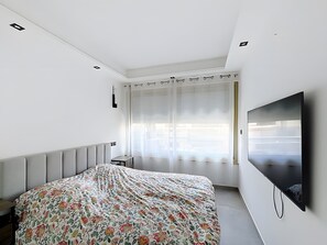 A bedroom with a bed, a TV, a window with blinds, and a radiator. - Apartment 'Appartement 2 Pièces Cannes' with Sea View, Wi-Fi and Air Conditioning (Cannes)