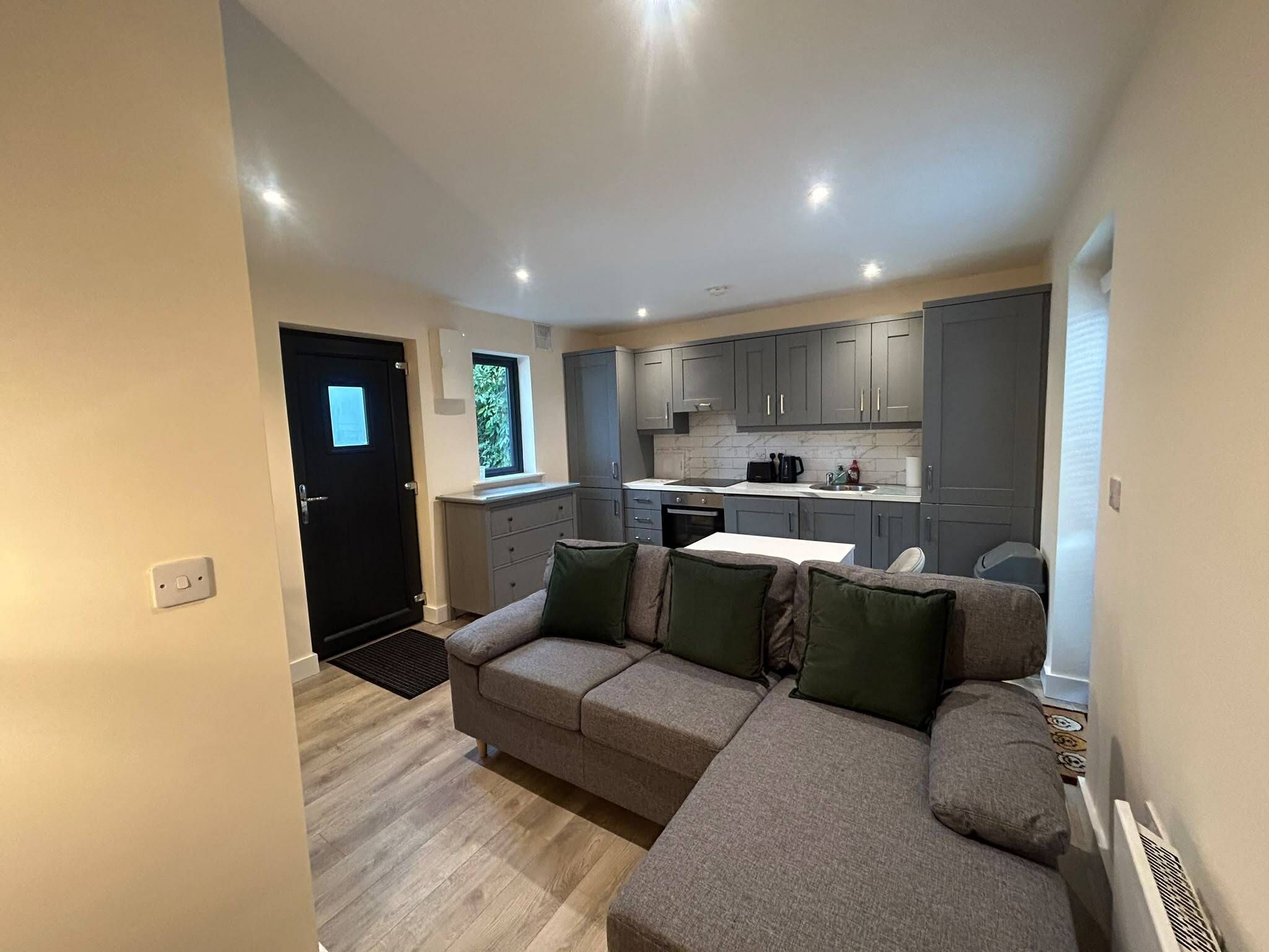 A compact living space with a sofa, a small kitchen area, and a door leading to another room.