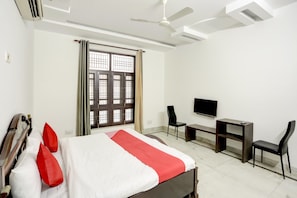 Une chambre d’hôtel équipée d’un lit, d’un bureau, d’une chaise, d’une télévision et d’un ventilateur de plafond.