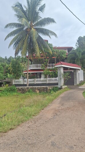 Una casa de dos pisos con techo rojo, cerca blanca en forma de estacas y una palmera en primer plano.