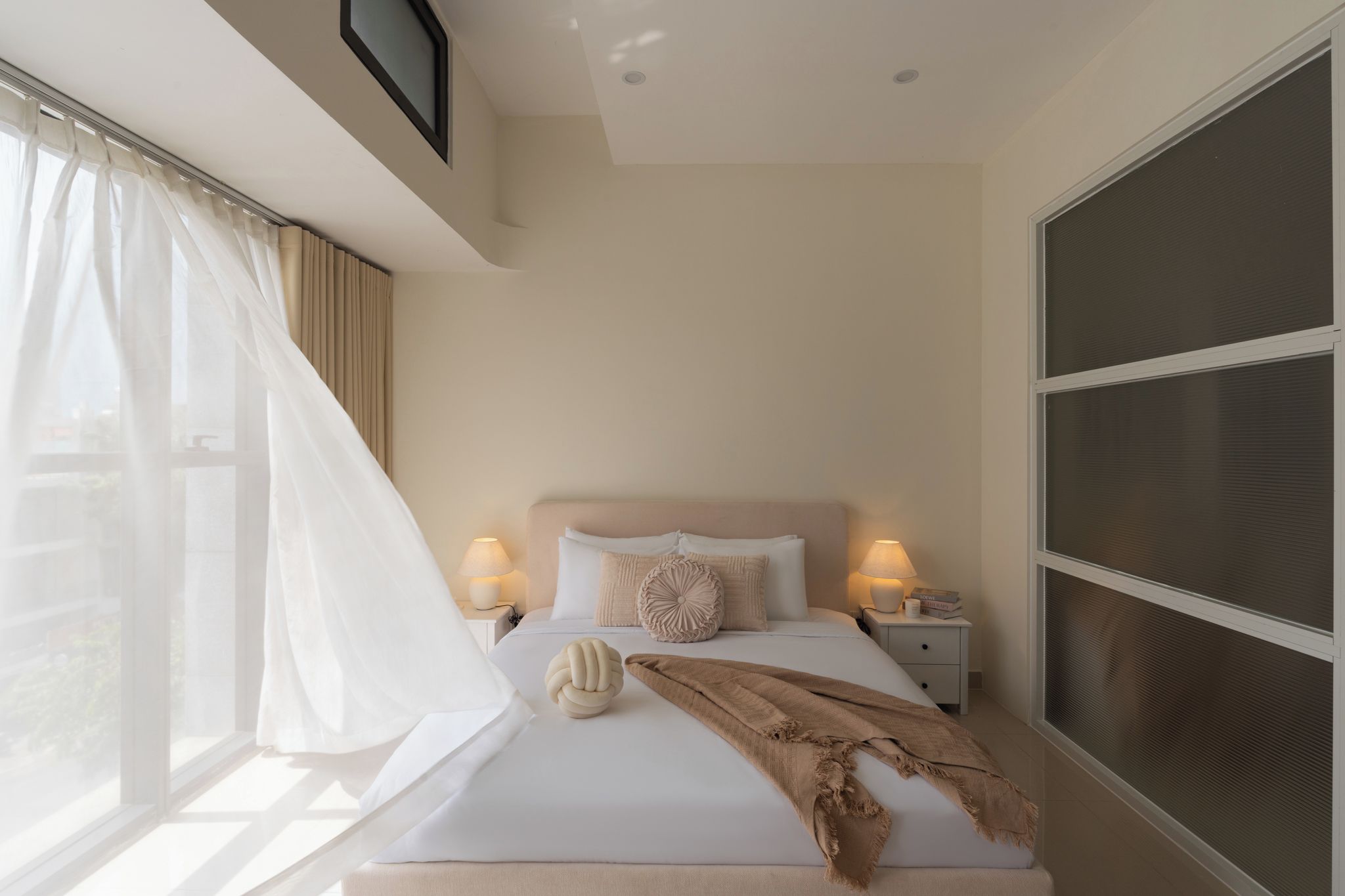 Una camera da letto con un letto, lampade sui comodini, una finestra con tende e una TV a muro.