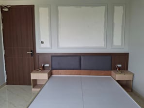 A bedroom with a bed, two bedside tables, a wooden wardrobe, and a door. - Ayodhya Blossom (Ayodhya)