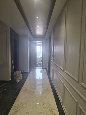 A hallway with a marble floor, doors on both sides, and a ceiling with recessed lighting. - Ayodhya Blossom (Ayodhya)