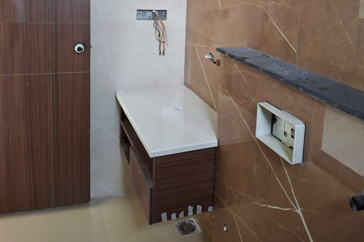 A bathroom with a wooden door, a white sink, a marble wall, and a shelf.