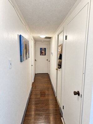 Passadís amb sòl de fusta, parets blanques i portes a banda i banda.