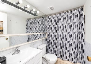 Une salle de bain avec un meuble-lavabo blanc, des toilettes et un rideau de douche orné d’un motif abstrait noir et blanc.