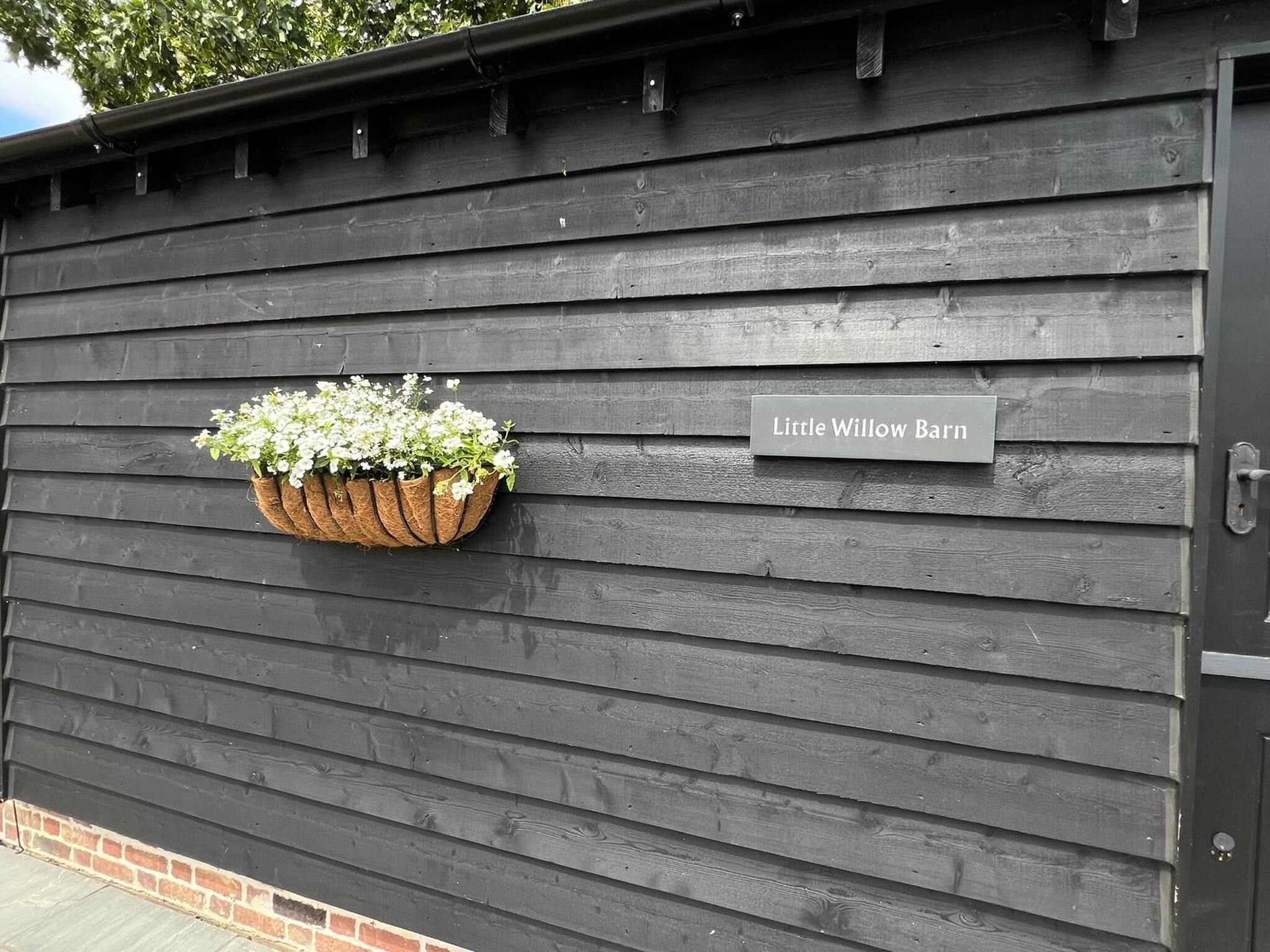 Eine schwarze Holzwand mit einem hängenden Blumenkorb und einem Schild, auf dem 'Little Willow Barn' steht.